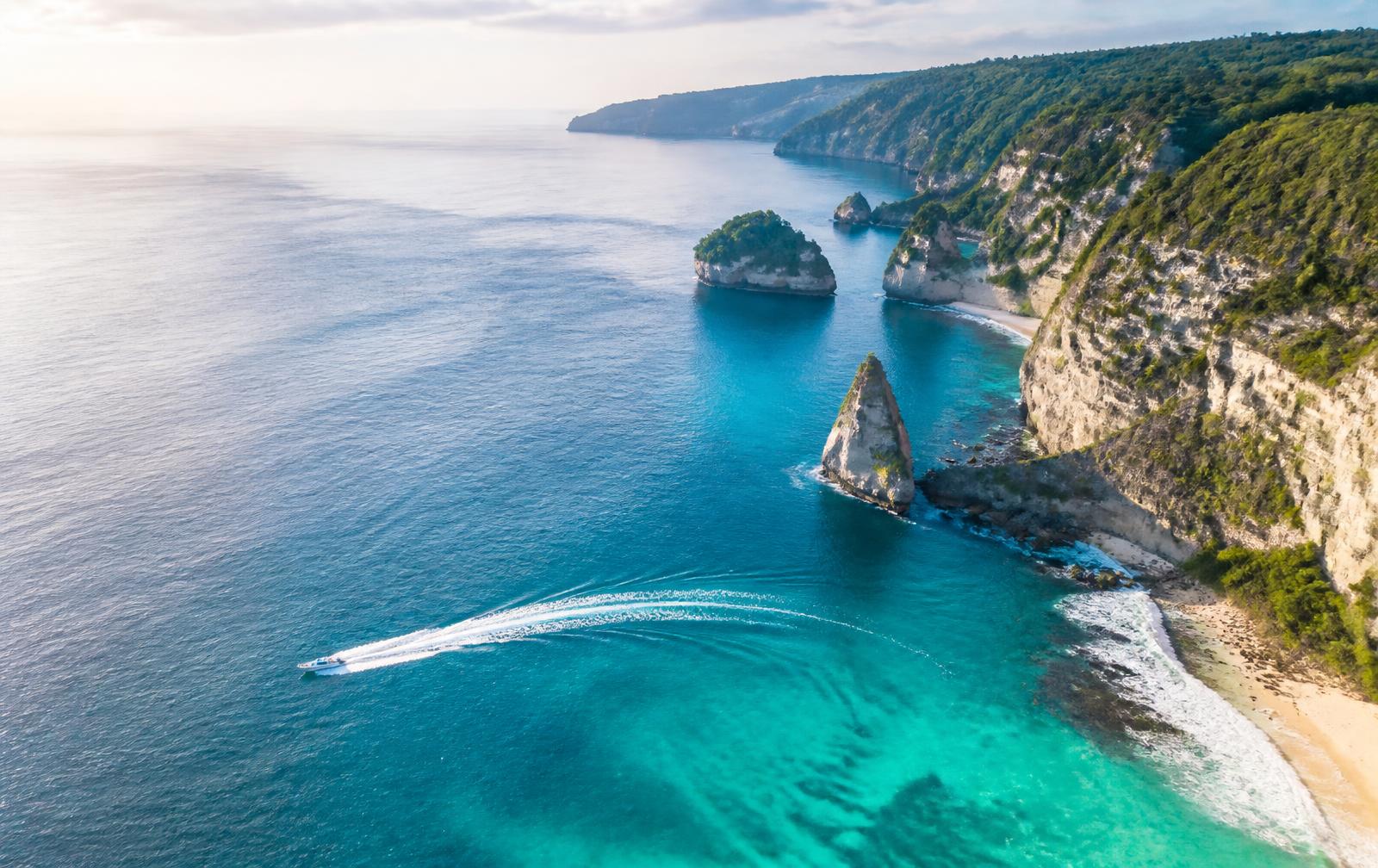 Fast boat crossing turquoise water beside the Nusa Penida cliffs